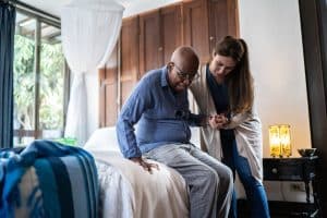 A nurse helping a nursing home resident get up from his bed. 