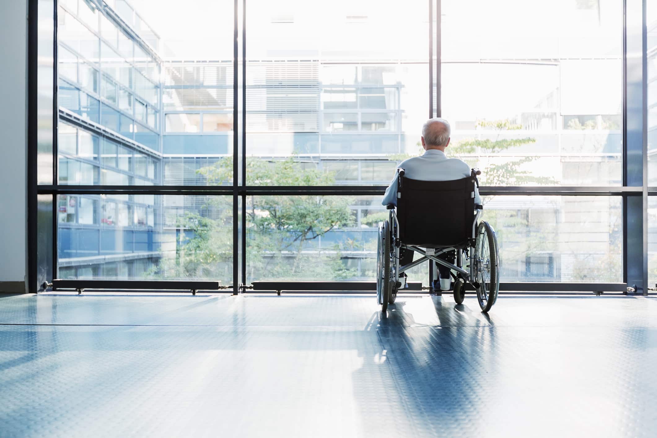 An elderly nursing home resident is left alone by a window.