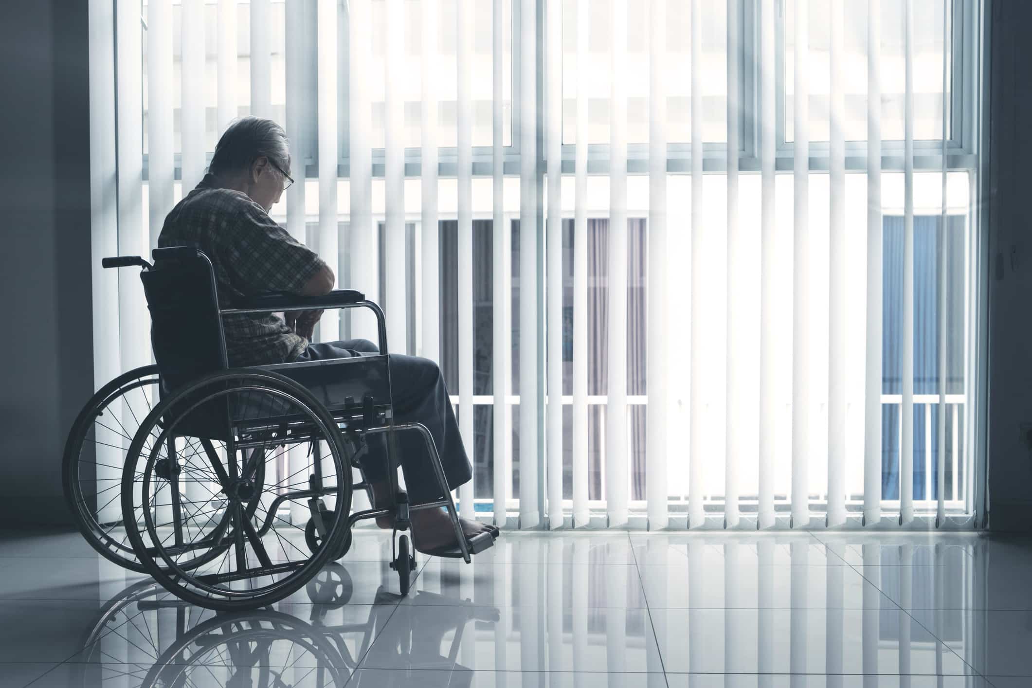 A sad old man looks out of a window while suffering from nursing home abuse