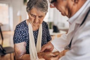 An older woman with bruises on her arm being taken care of by her doctor.