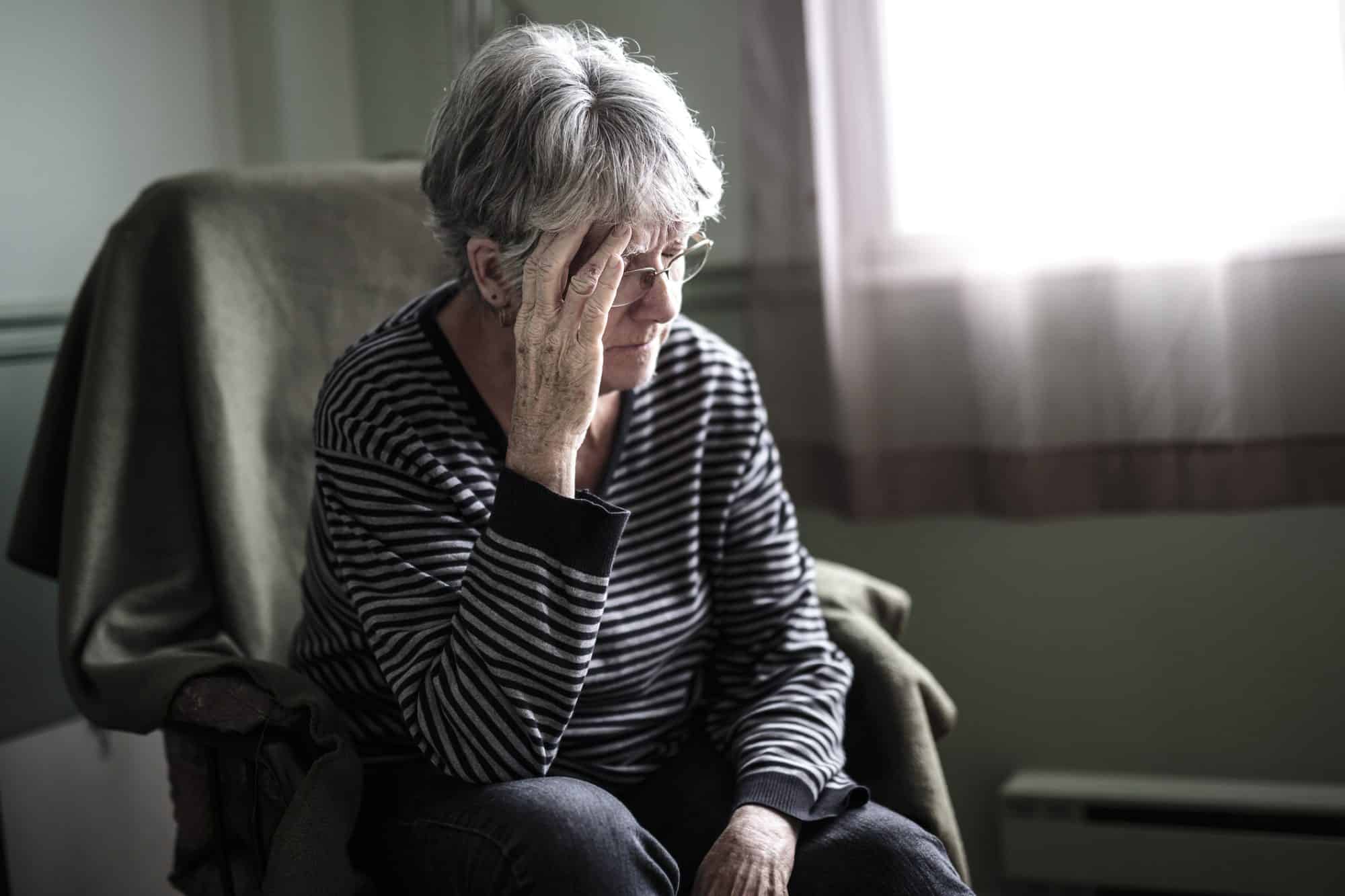 An elderly woman looking upset sitting in her nursing home.