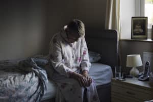 Depressed elderly woman sitting on a bed in the dark in a nursing home room