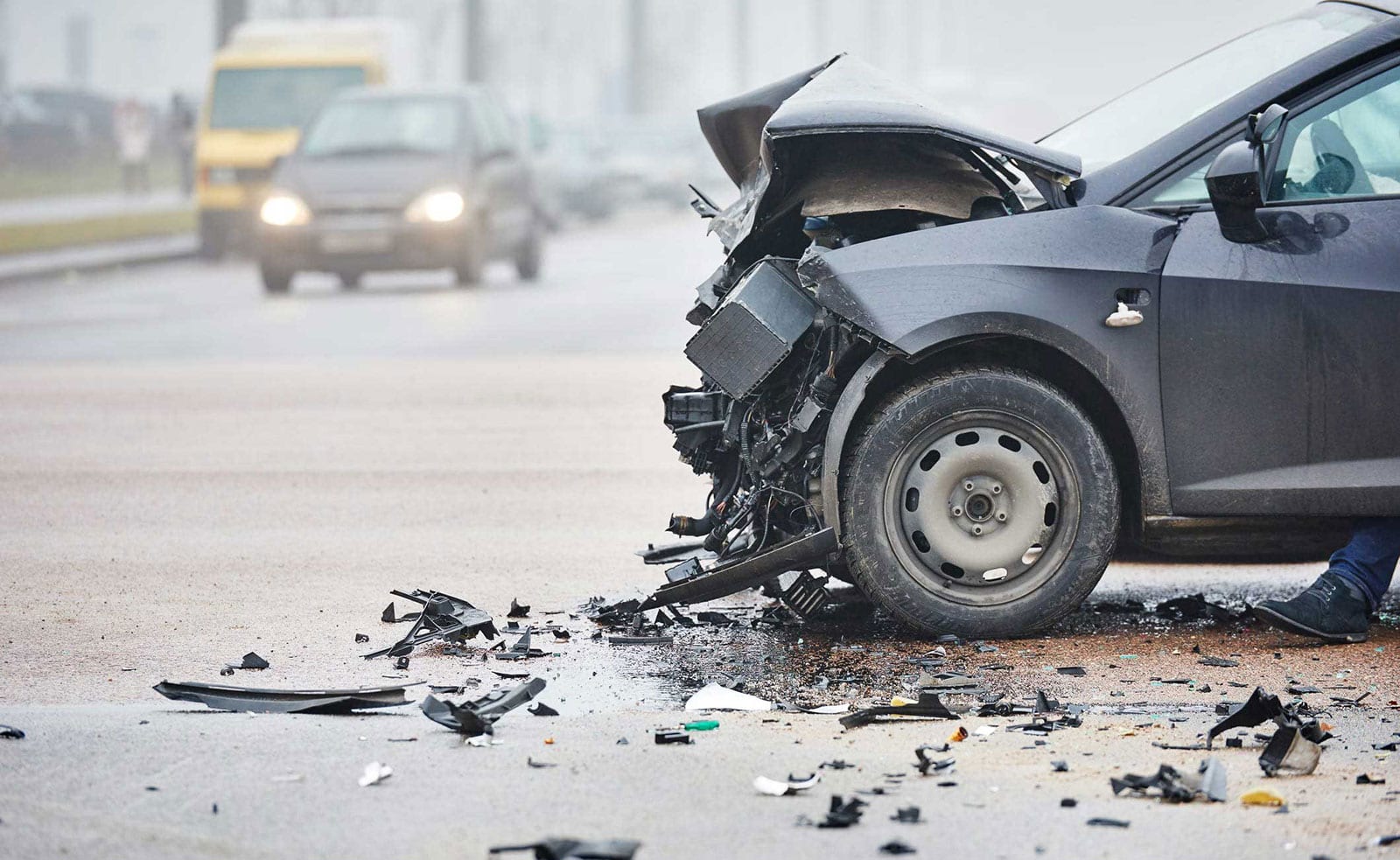 A car with severe front-end damage after a collision on a foggy road.