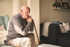 An elderly man sits alone trying to deal with the weight of financial burdens.