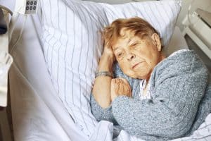 An elderly woman laying in her bed looking upset.