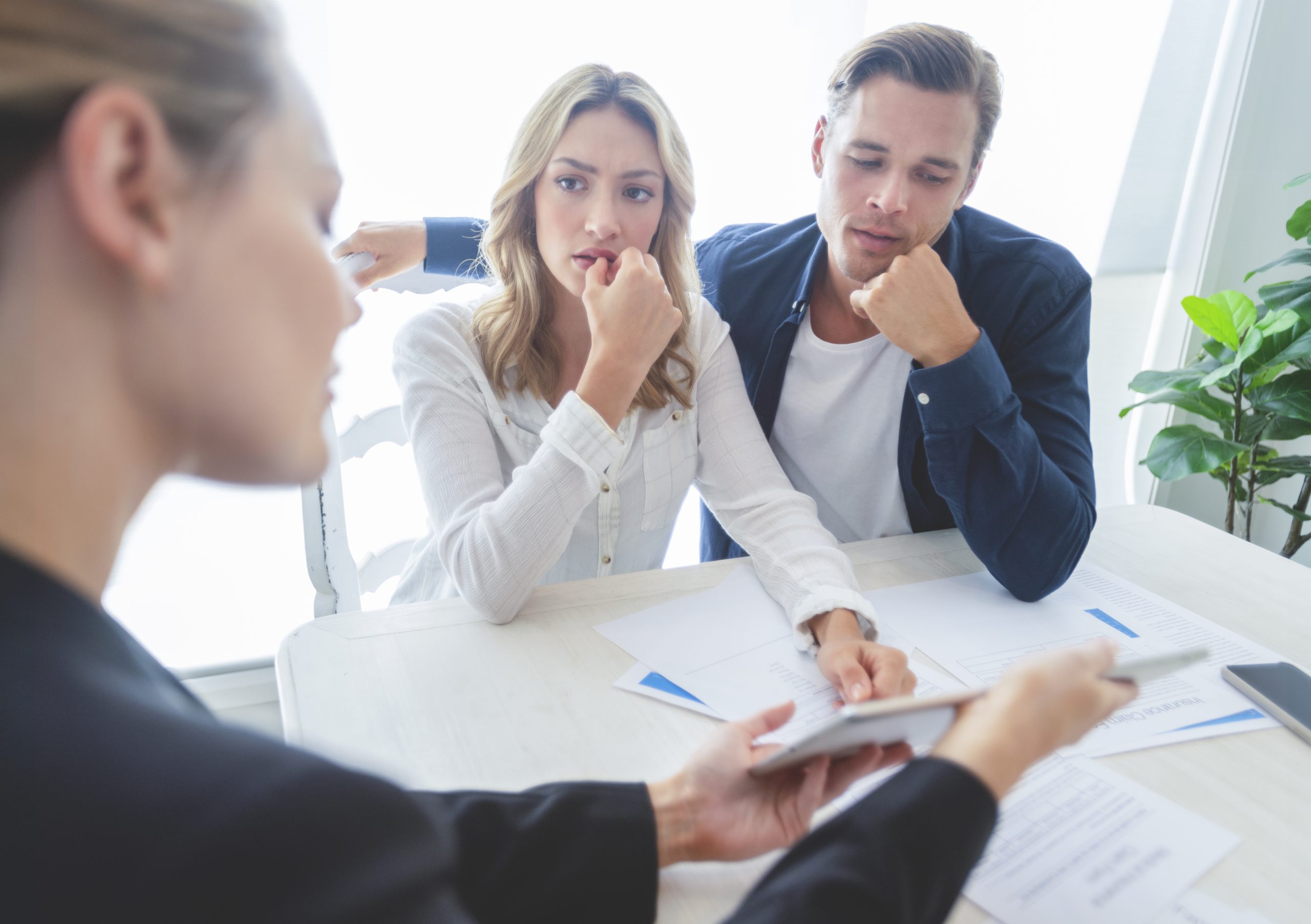 A concerned couple consulting with a lawyer at a table and reviewing documents together.