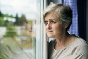 An older woman with a black eye staring out her window