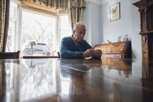 An elderly man looking worried while sitting alone at a table.